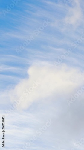 White clouds moving across bright blue sky. Vertical
