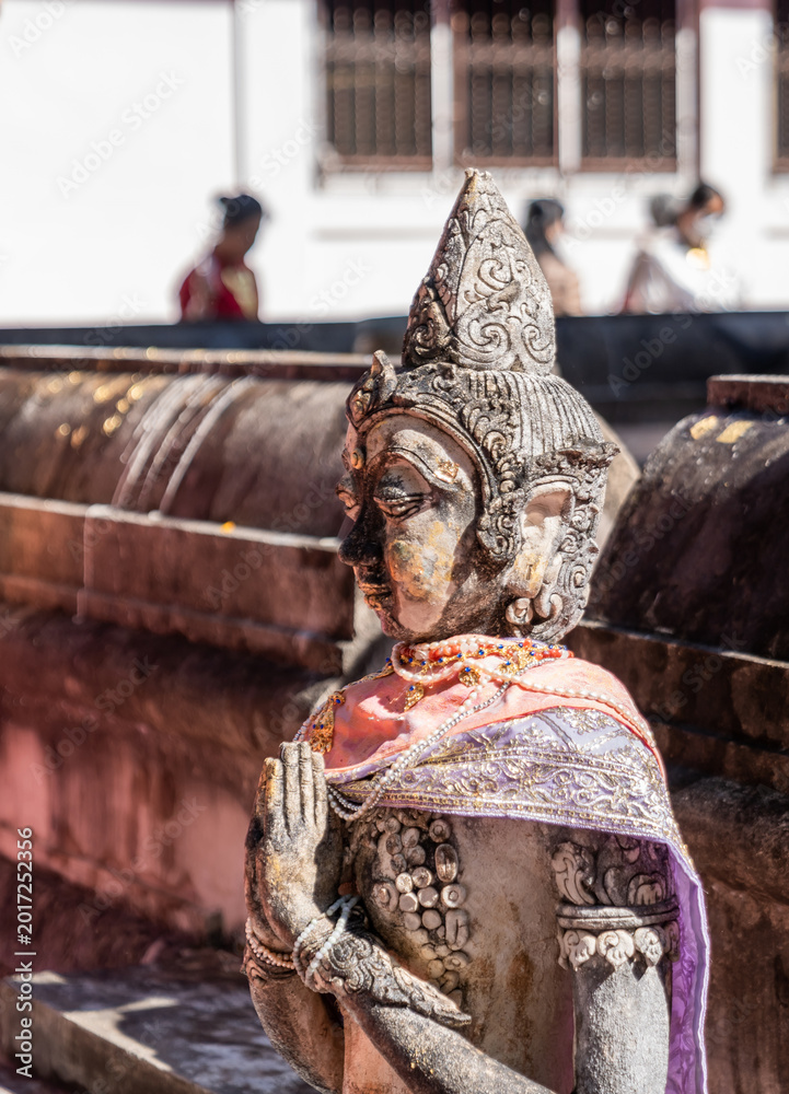Fototapeta premium Weathered female guardian figure stands within a sacred temple site surrounded by historic stone structures and cultural heritage architecture.