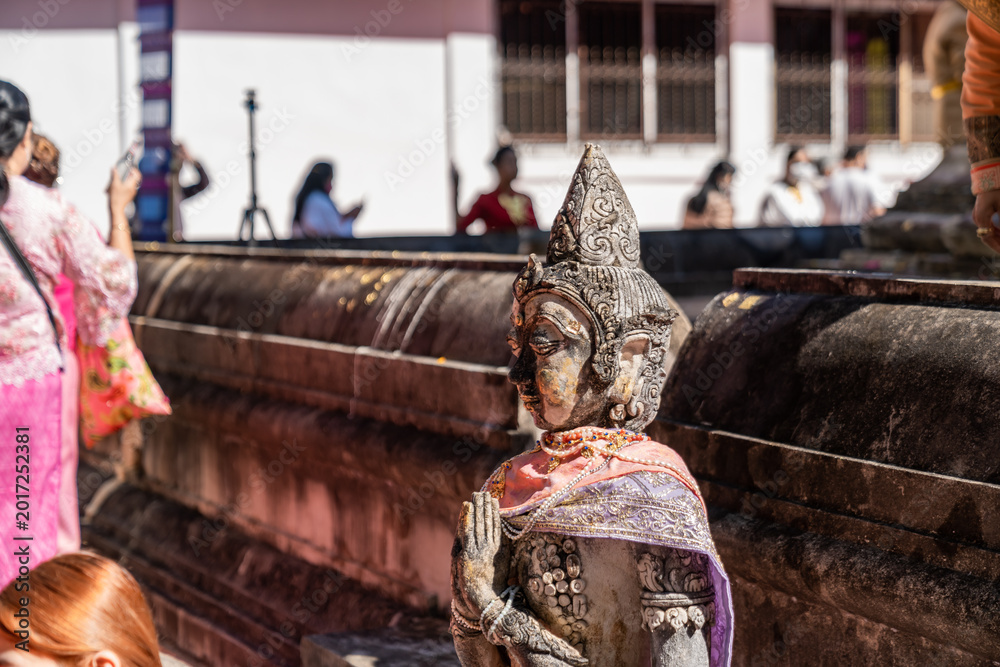 Fototapeta premium Weathered female guardian figure stands within a sacred temple site surrounded by historic stone structures and cultural heritage architecture.