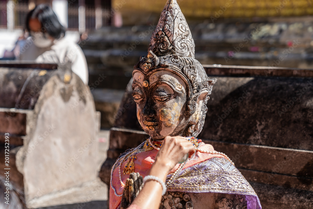 Fototapeta premium Weathered female guardian figure stands within a sacred temple site surrounded by historic stone structures and cultural heritage architecture.