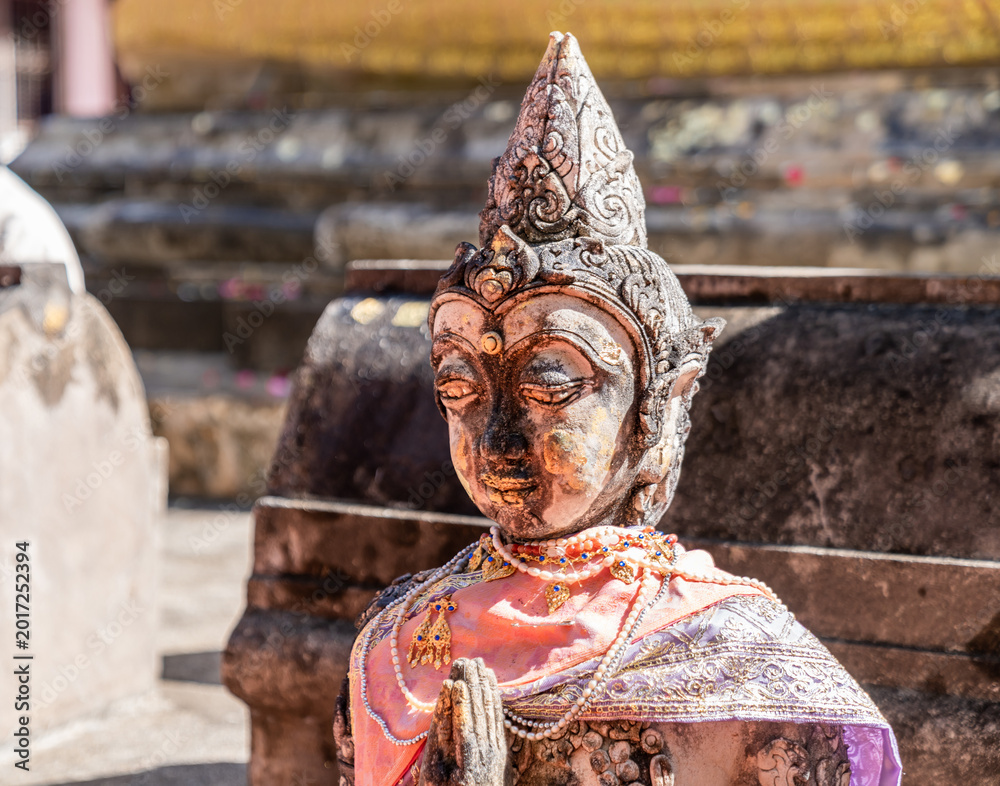 Fototapeta premium Weathered female guardian figure stands within a sacred temple site surrounded by historic stone structures and cultural heritage architecture.
