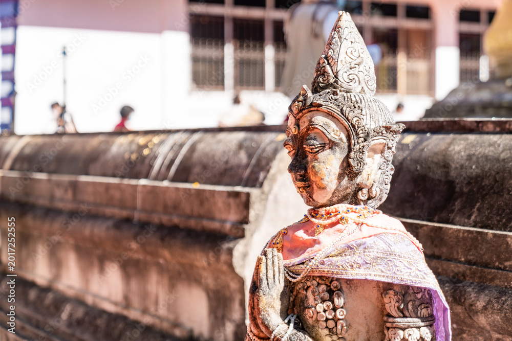 Fototapeta premium Weathered female guardian figure stands within a sacred temple site surrounded by historic stone structures and cultural heritage architecture.