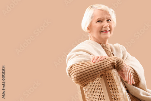 Schilderij op canvas Senior woman with shawl sitting in chair on beige background