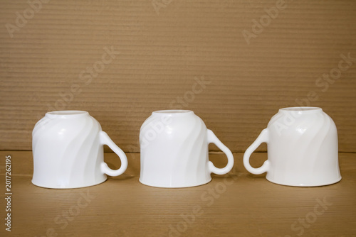 Minimalistic still life evokes a sense of pause, anticipation. Clean white mugs, turned upside down, rest on warm wooden surface - a quiet moment before a shared cup of tea or coffee.