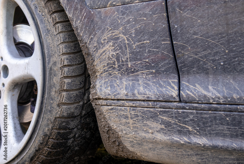 Obraz premium A car parked near a dirt road shows heavy dirt and mud on its body and tires after driving on an unpaved path under bright sunlight