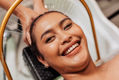 Smiling Southeast Asian woman enjoying aqua ring water halo scalp rinse at a Japanese head spa for relaxation, cleansing, and scalp hydration.