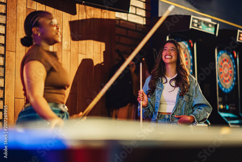 Tableau sur toile Young diverse women having fun playing pool in a bar, laughing and smiling, enjo