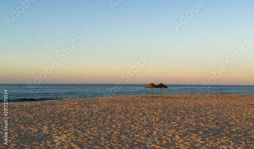 Wooden umbrellas on an empty sandy beach at sunset in low season