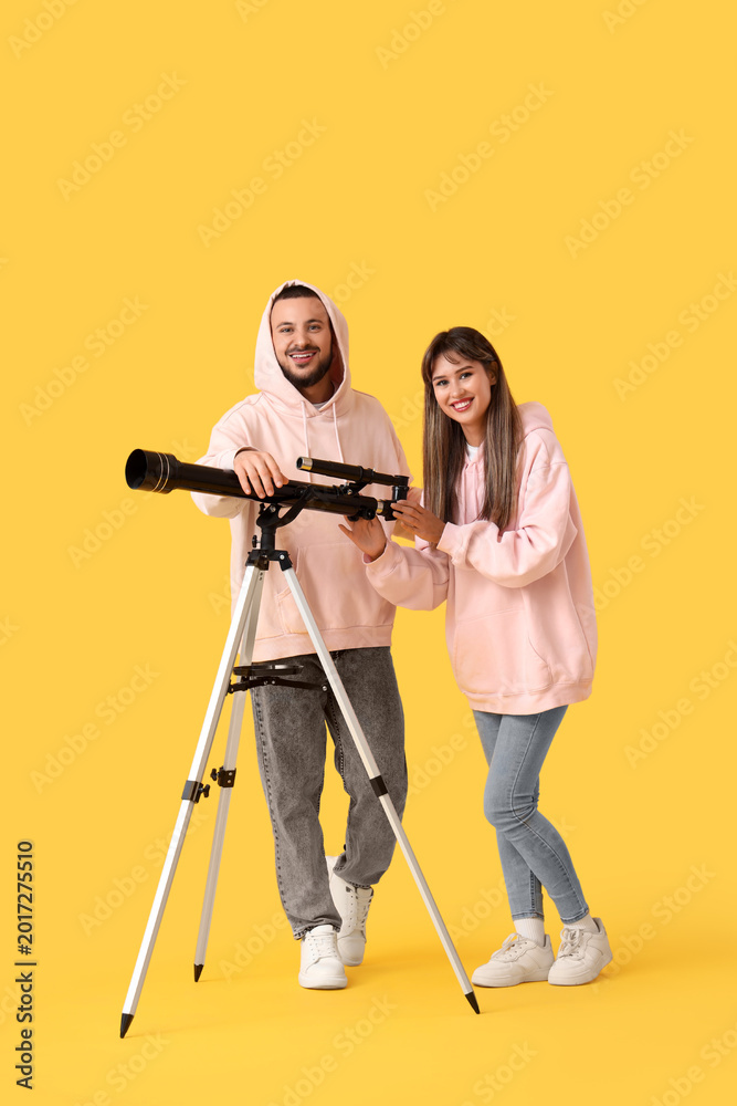 Fototapeta premium Young couple with telescope on yellow background