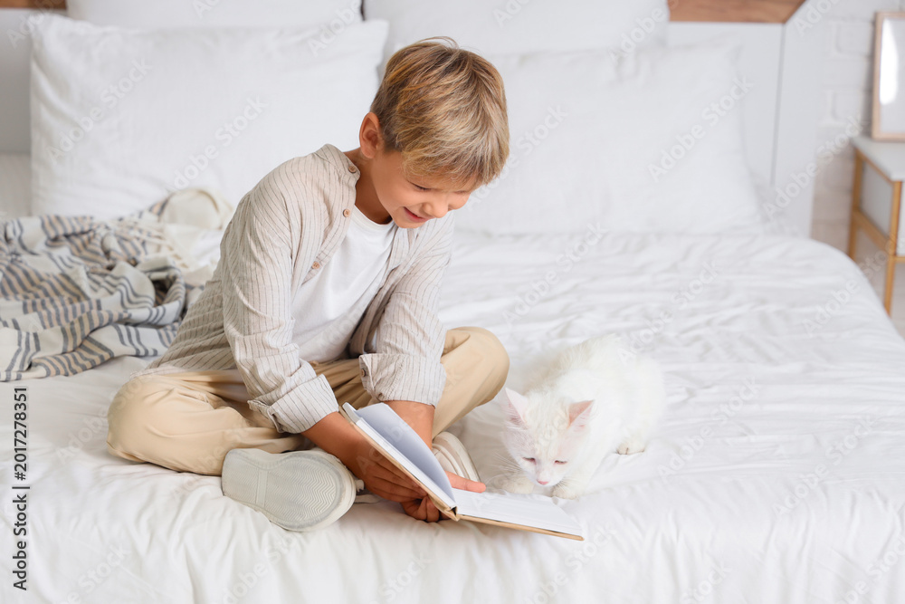 Fototapeta premium Little boy with cat reading book in bedroom