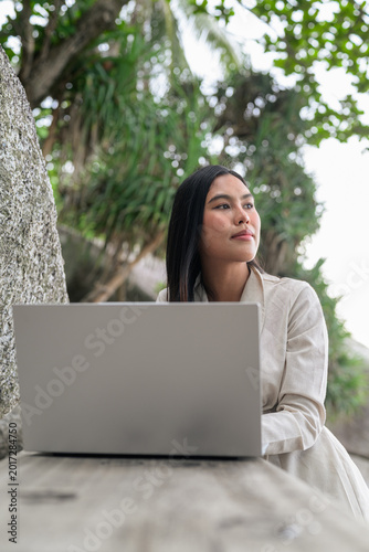 Successful Thai woman digital nomad in Phuket working on her laptop while enjoying a tropical remote work lifestyle in nature.