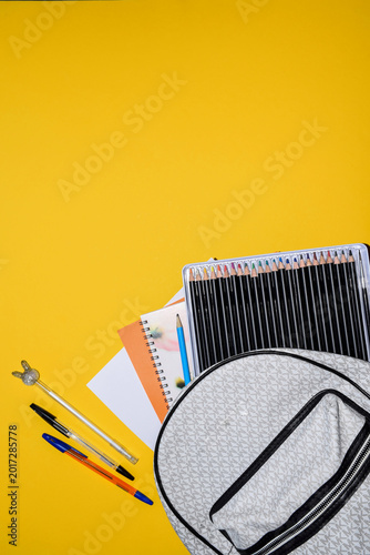 School Backpack with Colored Pencil Set Notebooks and Pens on Yellow Background with Copy Space