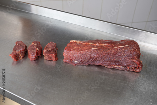 Perspective view of raw beef primal cut and three sliced steaks on stainless steel