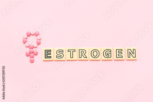 Symbol of woman made of hormonal pills with word ESTROGEN on pink background