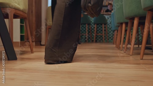 Closeup wooden floor walking businessperson shoes under chairs, soft ambient lighting, midcentury chairs and tables, polished wood planks, measured footsteps and steady pace, briefcase swing,