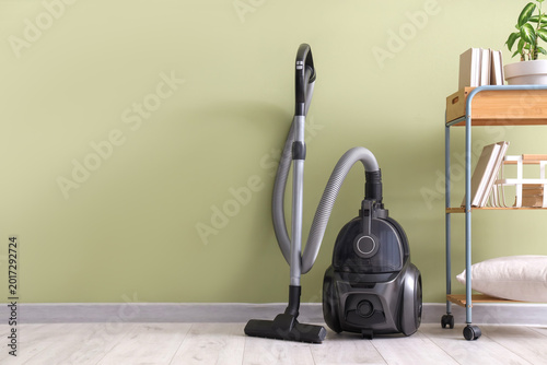 Obraz na plátne Modern vacuum cleaner and shelf unit near green wall in room