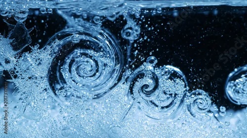 Close-up of swirling blue water creating dynamic spiral vortexes and bubbles, suggesting fluid dynamics and refreshment, dark background