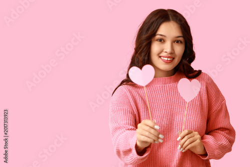 Beautiful young Asian woman with pink paper hearts on color background. Valen...
