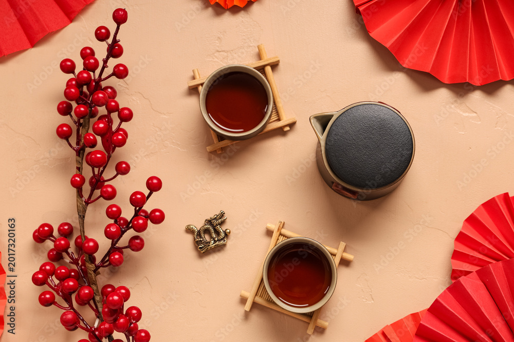 Fototapeta premium Teapot with cups of tea, berries and Chinese symbols on beige background. New Year celebration