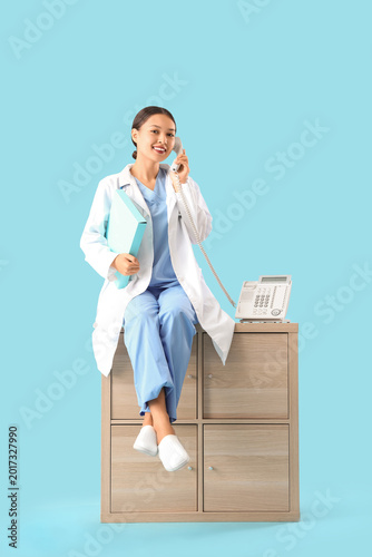 Female Asian doctor talking by telephone on blue background