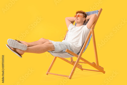Young man resting in deck chair on yellow background