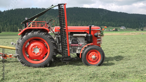 Tableau sur toile Vintage red agricultural tractor with side sickle bar mower in a green field