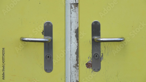 Symmetrical pair of modern metal lever handles on aged yellow painted wood surface
