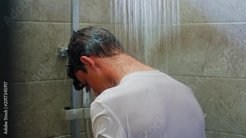 A teenage boy sits in the shower alone water is pouring on him, with his head in his hands, upset and overwhelmed. The kid is feeling upset, emotional, and mentally struggling