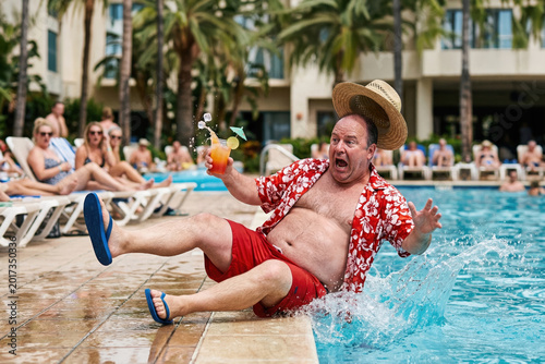 Clumsy middle aged man slipping and falling into resort swimming pool with cocktail