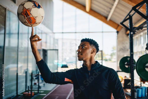 Fit young black sporty man in sportswear smiling while spinning a ball on his fingertip during a break between workouts in a gym