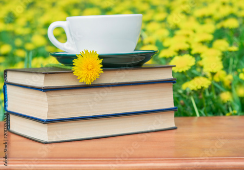 Stack of books with tea cup and dandelion on carved wooden table with floral background