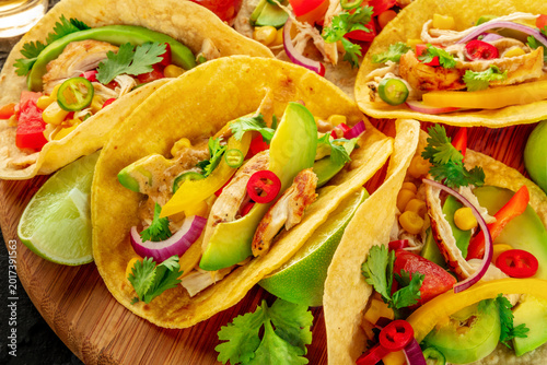 Mexican tacos with pulled chicken, avocado, chili peppers, and limes, a close-up