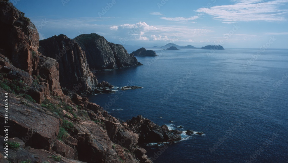 Obraz premium Dramatic Coastal Cliffs Overlooking a Serene Blue Ocean Under a Cloudy Sky.