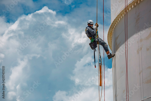Male worker rope access industrial working at height tank oil wearing harness, helmet safety equipment rope access inspection of thickness