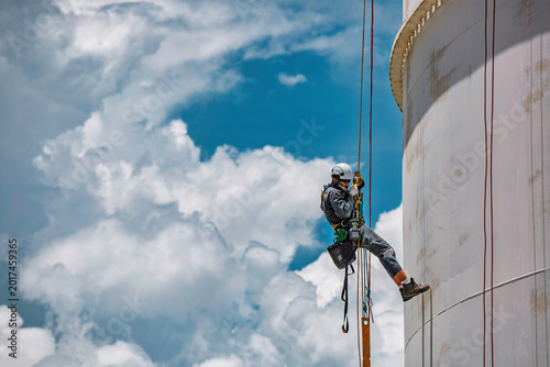 Male worker rope access industrial working at height tank oil wearing harness, helmet safety equipment rope access inspection of thickness