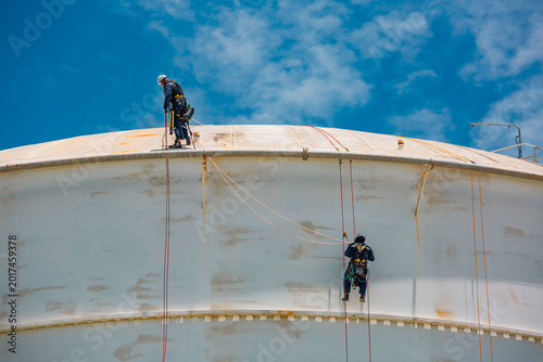 Male worker rope access industrial working at height tank oil wearing harness, helmet safety equipment rope access inspection of thickness