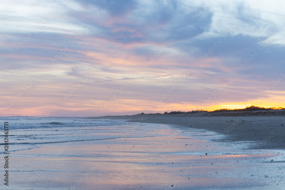 Fototapeta premium Gentle waves and a glowing sky in shades of pink and blue create a serene atmosphere
