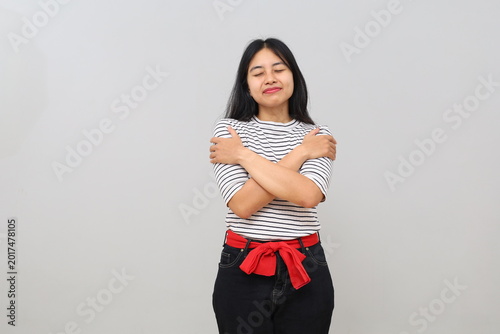 Canvastavla A young Asian woman smiling happily, peacefully, calmly and contentedly, proud of herself, hugging herself, closing her eyes, isolated on a white background
