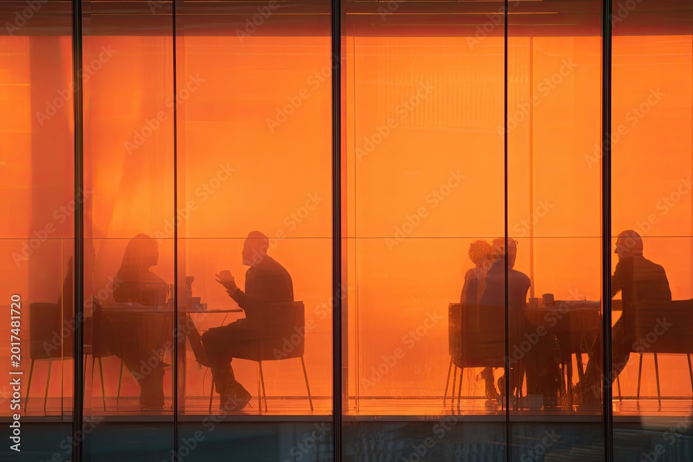 Naklejka premium Silhouetted figures gather in a warmly lit, modern office space