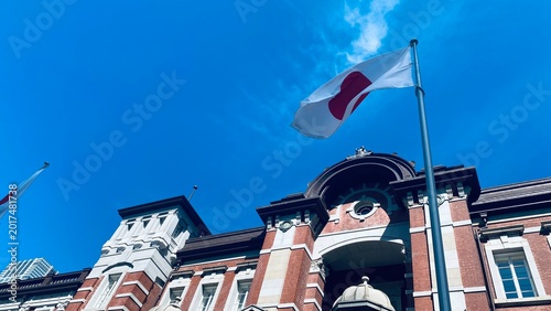 Fotografía Japanese Flag Waving in Front of Tokyo Station Under Blue Sky