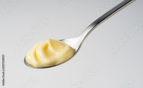 Creamy mayonnaise with elegant swirl on a stainless steel spoon, thick yellow sauce condiment on light gray background
