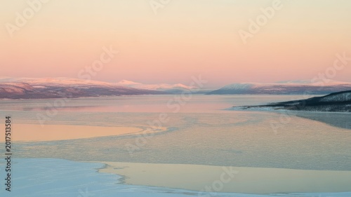 Serene sunset over calm lake with distant mountains and clear sky