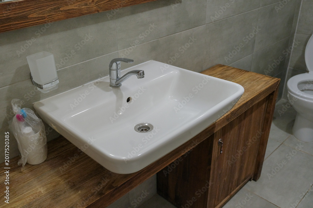 Fototapeta premium Modern faucet and water flow. Stylish white sink in a light interior. Chrome steel tap. Domestic Appliances. Gray clean bright bathroom. Household equipment. Grey vanity with tiled wall. Home interior