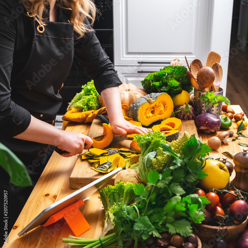 фотографія Woman slicing pumpkin on wooden board following digital recipe on tablet