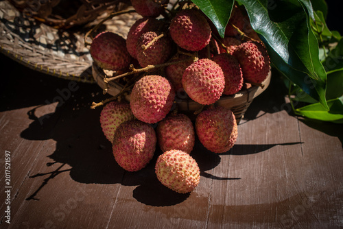 Tableau sur toile Fresh red lychees with green leaves in a wicker basket on a wooden table