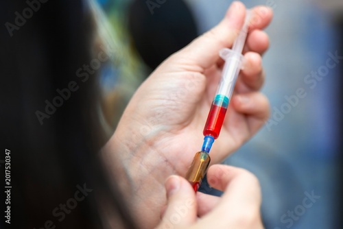 Female hands drawing bright red liquid medicine from an ampoule into a disposable syringe.