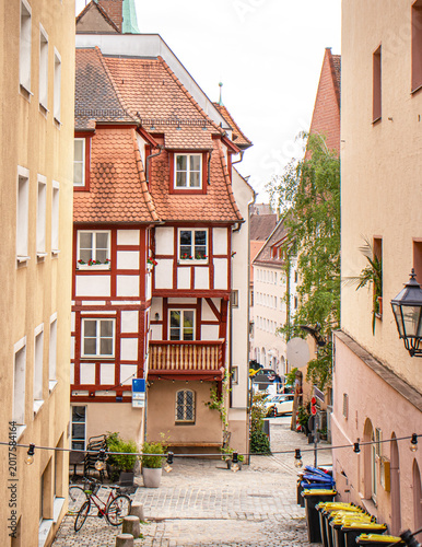 Charming narrow cobblestone street in a historic European old town featuring traditional half-timbered houses with red tile roofs and floral window boxes