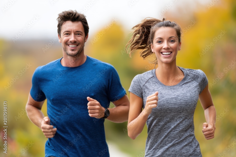 Obraz premium Young couple jogging in nature, smiling and staying active together outdoors on a sunny day
