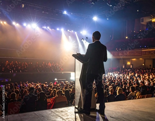 Speaker addresses large audience on brightly lit stage