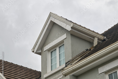 light grey stucco house wall with white window and brown tiled roof, close-up of home construction and property maintenance
